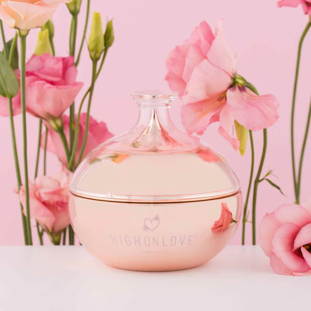 Pink bottle of Body Butter by High On Love against a flower background.