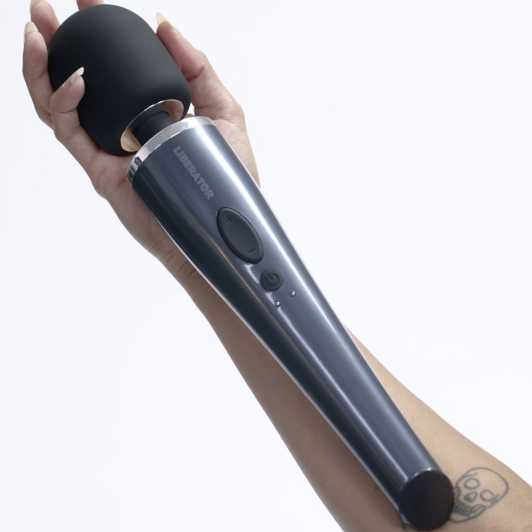 An arm holding a black DeJour Vibrating Wand bedroom toy by Liberator showing it's the size of a forearm on a white background.