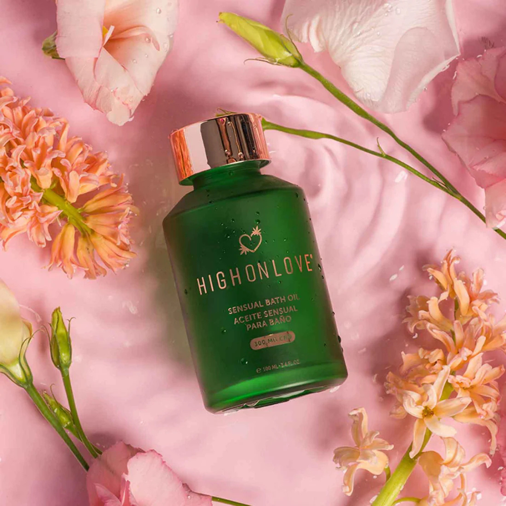 Green bottle of Elevated Bath & Body Oil by High on Love for relaxation laying on water with flowers.