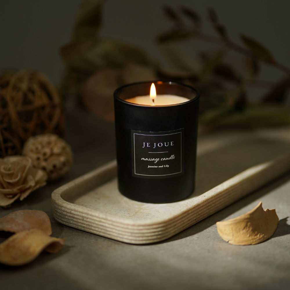 A black massage candle by Je Joue on a board surrounded by spices.