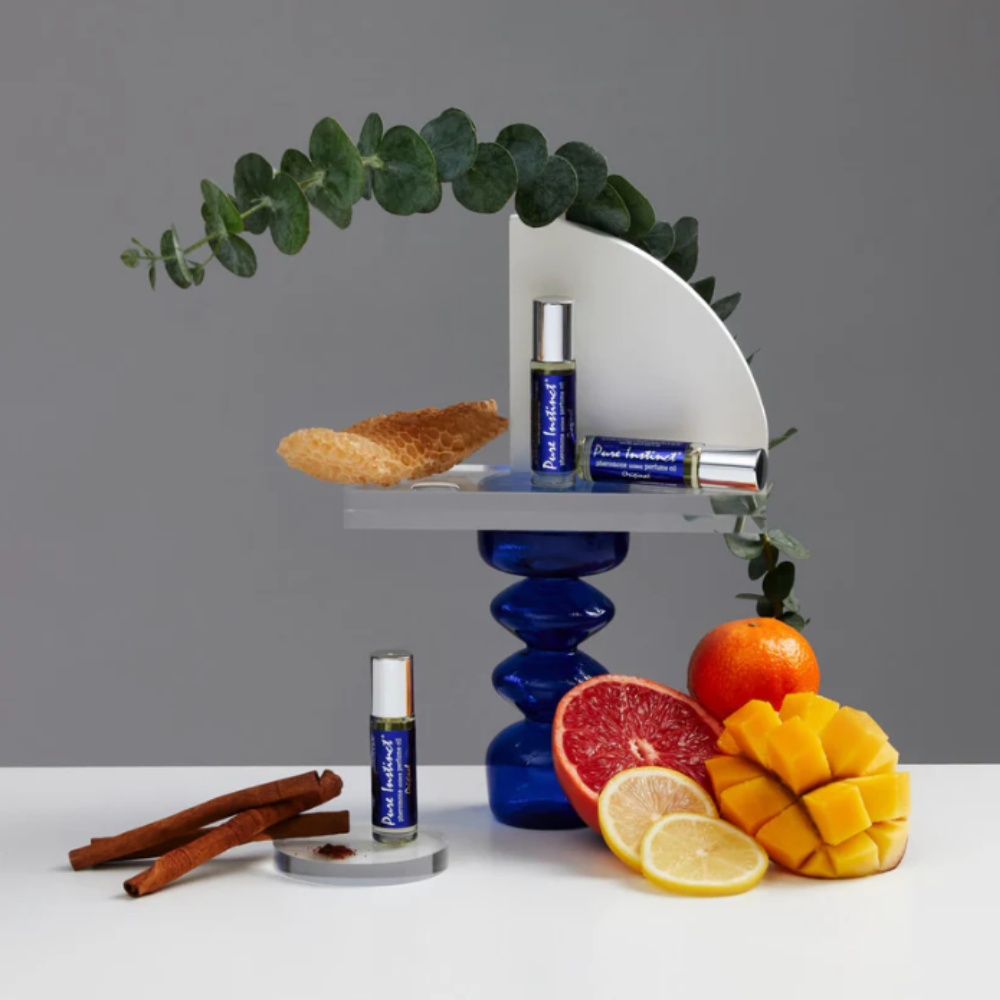 Three blue phromone rollerballs by Pure Instinct Roller - For Her stacked up against fruits and spices.