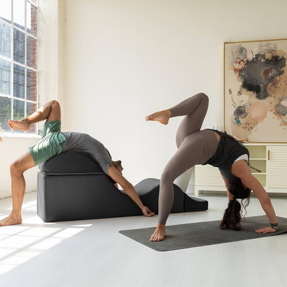 Two people practicing yoga with the black aria chaise in a bright room with large windows.