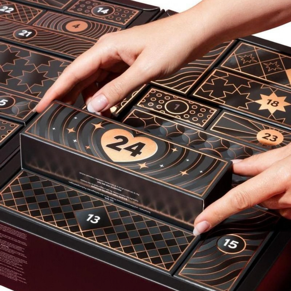 A hand pulling out box #24 out of a  black Luxury 24-Day Advent Calendar for couples.