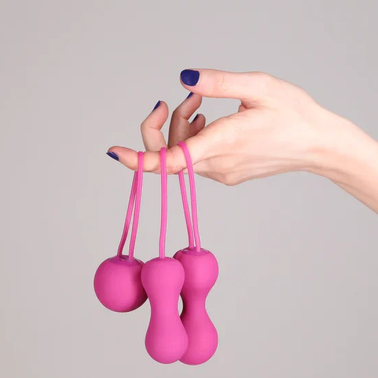 Three pink silicone kegel weights held by a hand against a gray background