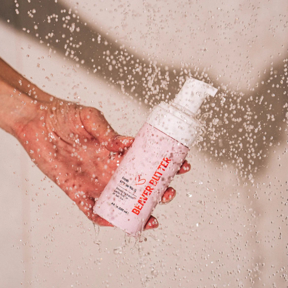 A pink bottle of Beaver Butter Intimate Wash by ECN held in splashing water.