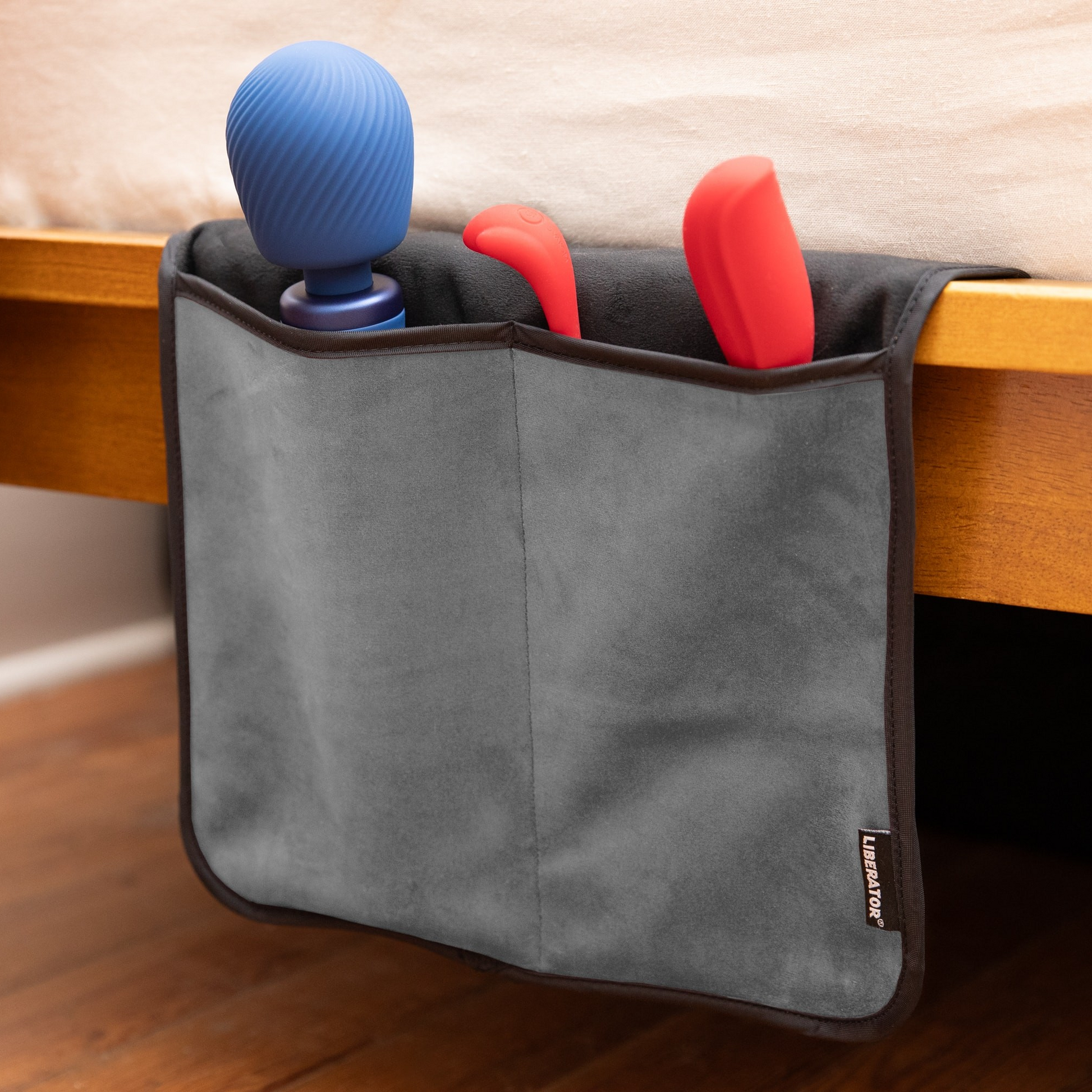A grey bed caddy by Fascinator haning on a bed holding toys.