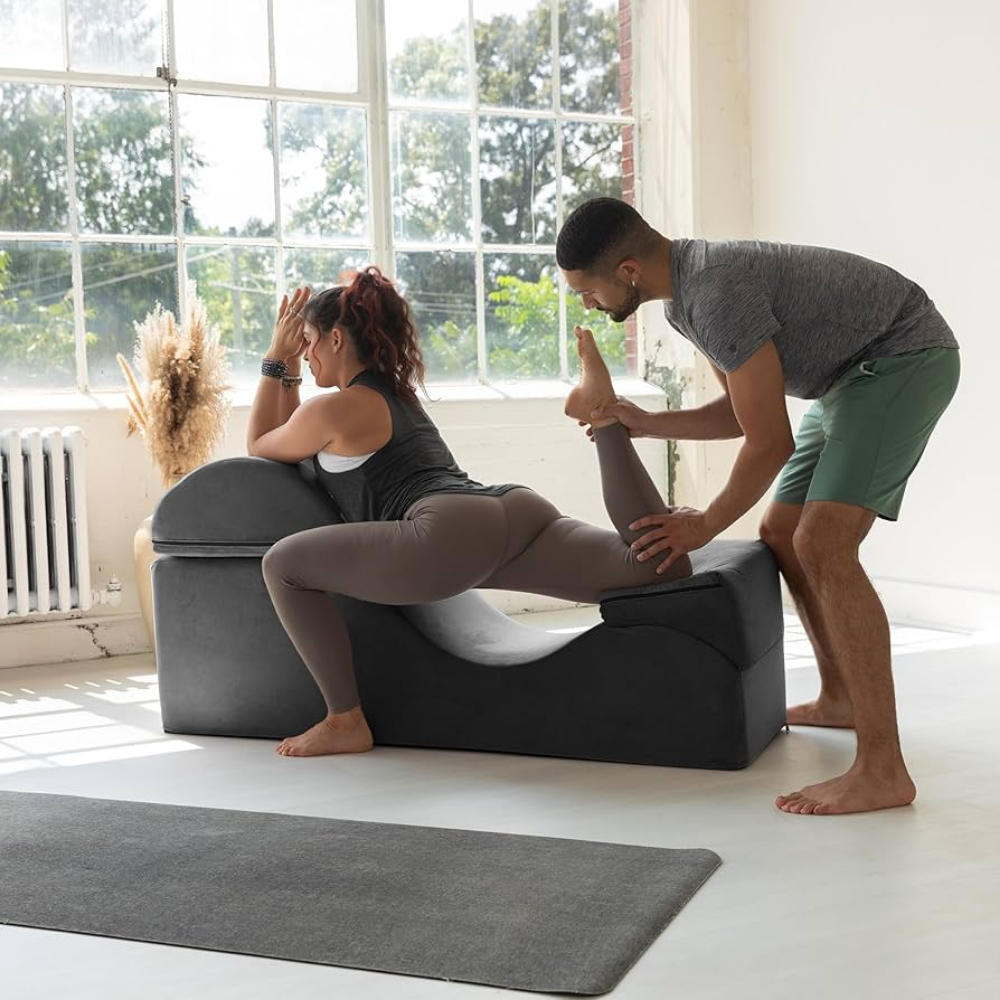 A black Aria Flip Chaise by Liberator unfolded into a chaise with a couple doing yoga moves on it.
