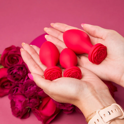 Two hands holding a set of three red Bouquet Anal Trainers in different sizes in front of roses.