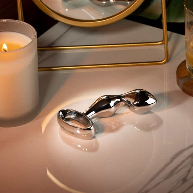 A silver Cassa plug against a white background sitting on a white table next to a candle.