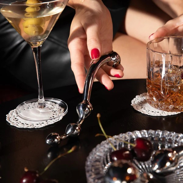 A hand holding stainless steel Corda Wand on a table with cocktails.