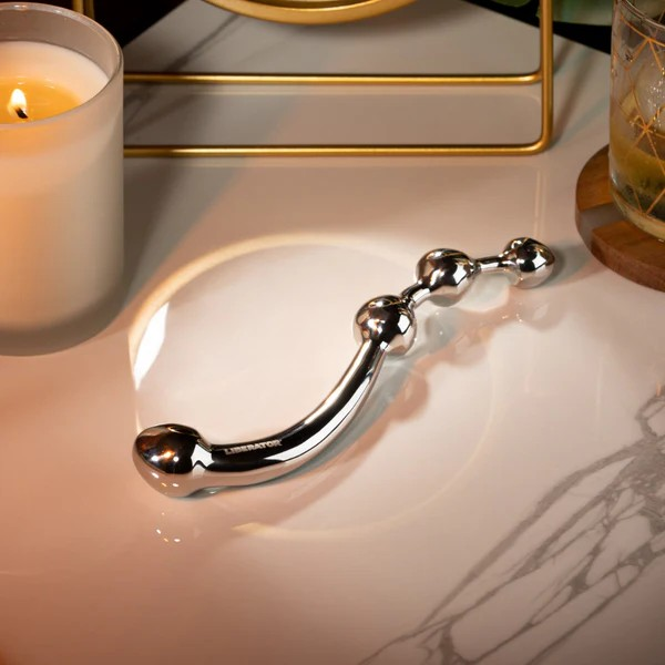 A stainless steel Corda Wand sitting on a white table next to a candle.