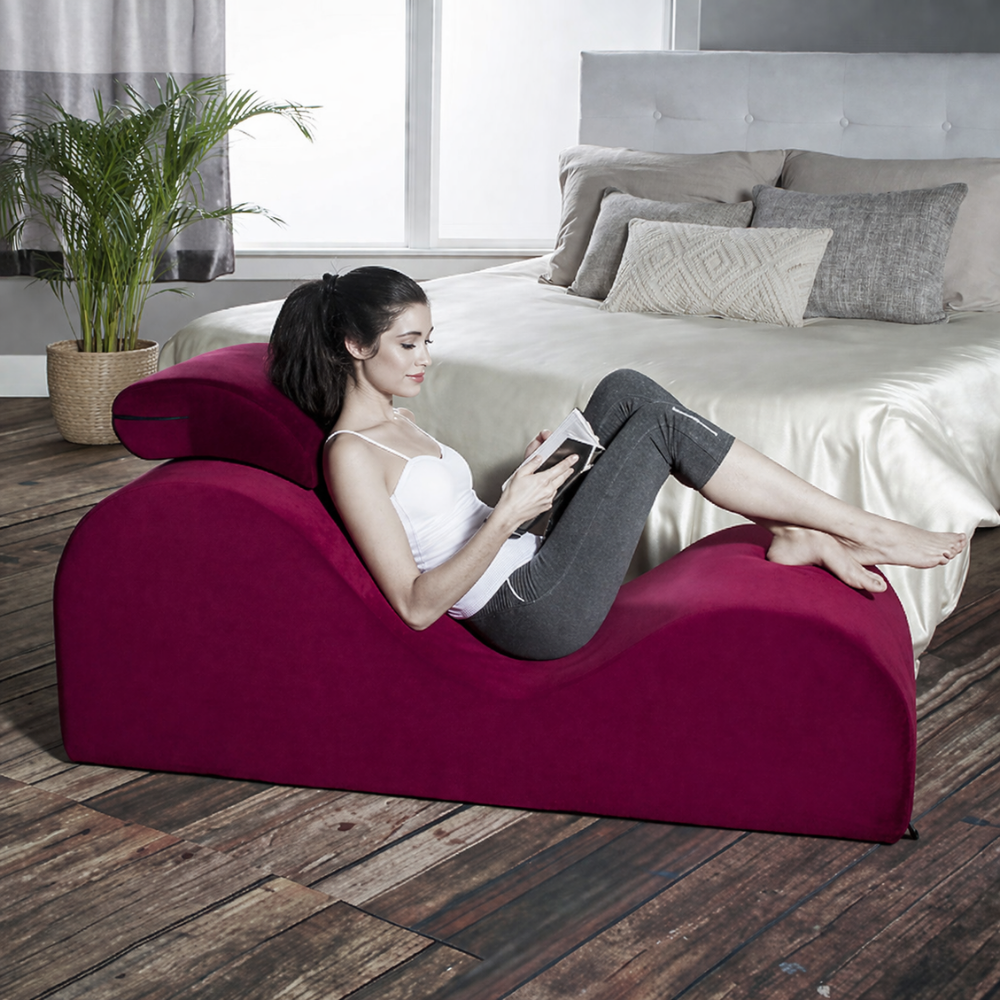 Woman reading a book on a esse lounger curved red chair in a bedroom.