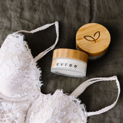 Two white jars of Edible Massage Cream by Evree sitting next to a piece of white lingerie.