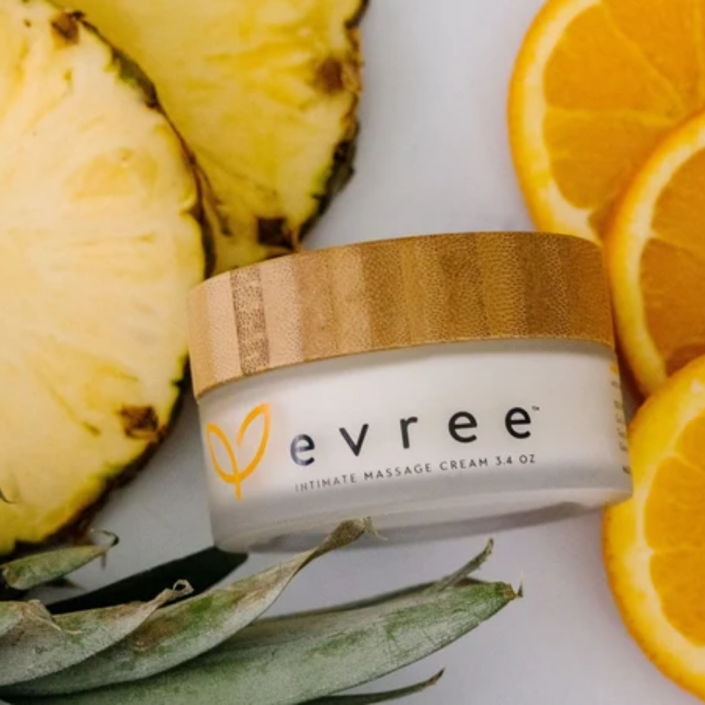 A white jar of Edible Massage Cream by Evree sitting among some pineapple and orange slices.