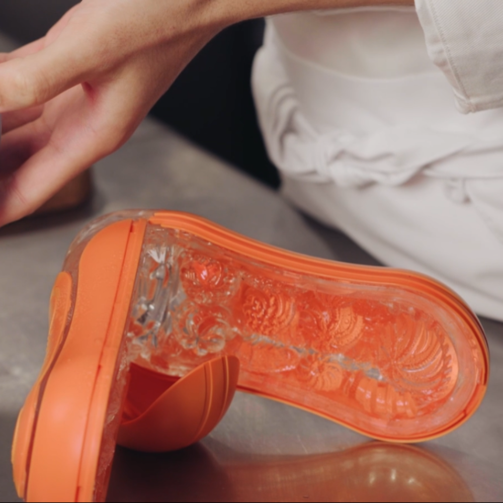 Close-up of a orange and clear male sleeve open to dry on a neutral background