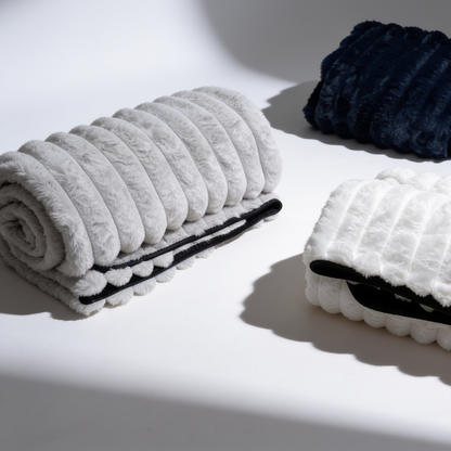 A white, grey and black Fascinator Luxe Splashproof Fur blanket rolled up sitting against a white background.