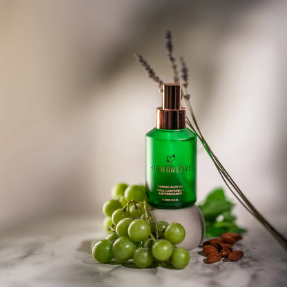 A green bottle of Firming Body Oil, Bath & Body by High On Love sitting next to some grapes and lavender.