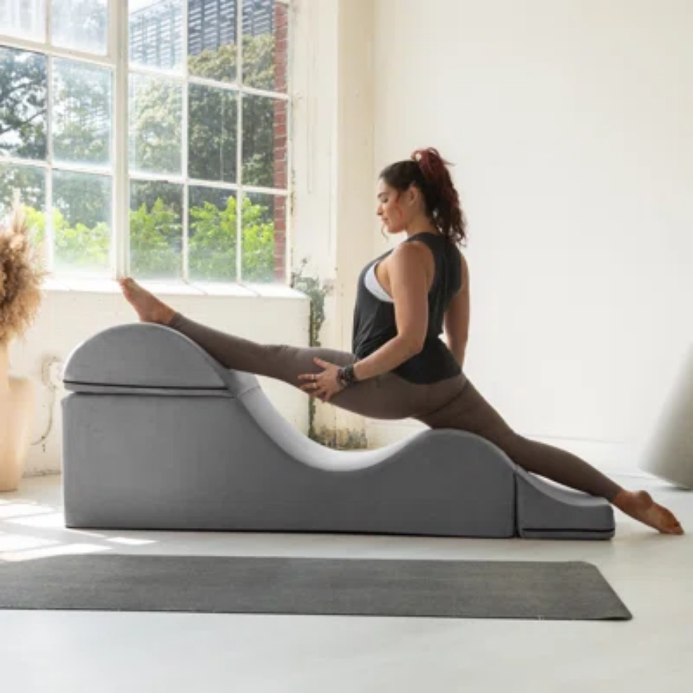 Woman using a grey aria chaise in a bright room with large windows.