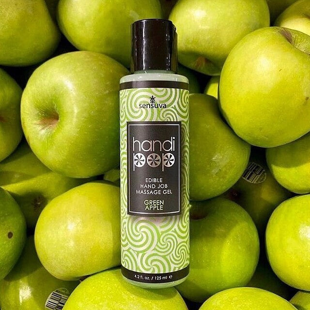 A green and white bottle of Handipop green apple Eidble Hand job massage gel by Sensuva against a background of green apples.