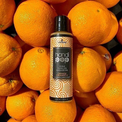 A orange and white bottle of Handipop orange creamsicle Eidble Hand job massage gel by Sensuva against a background of oranges.