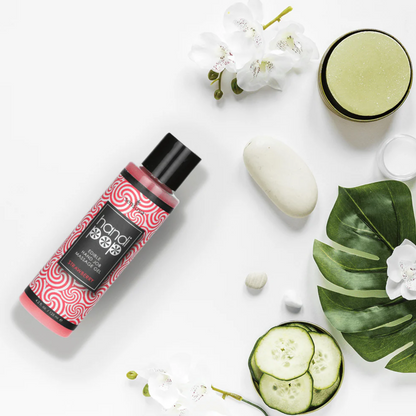 A red and white bottle of Handipop strawberry Eidble Hand job massage gel by Sensuva on a white background next to flowers and cucumber slices.