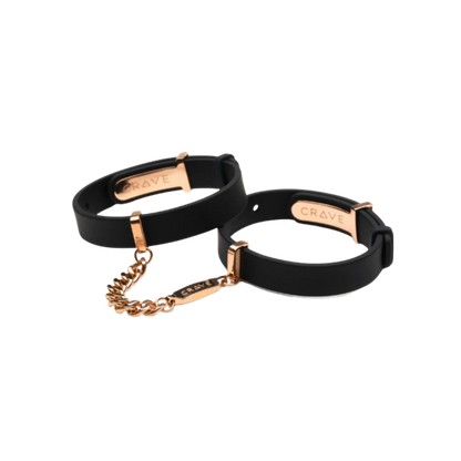 A set of black cuffs with a gold chain.