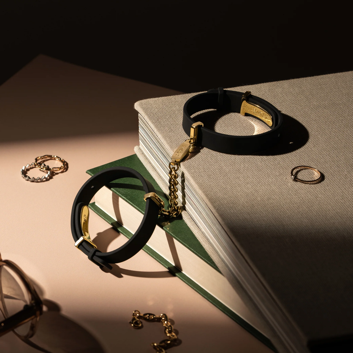 A set of black cuffs with a gold chain sitting on a table with books and jewerly.