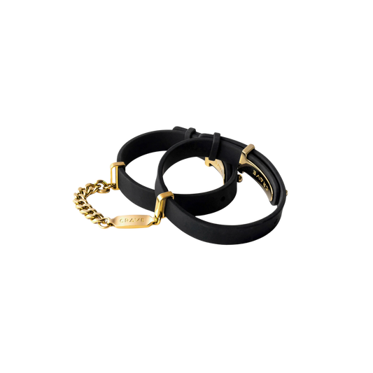 A set of black cuffs with a gold chain.