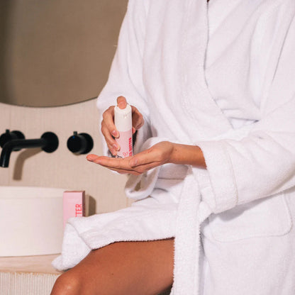 A person in a white robe using a bottle of ingrown hair serum by Beaver Butter.