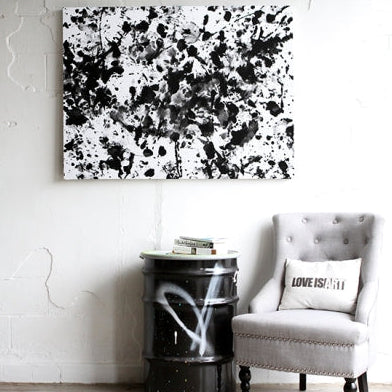 Bold Black black and white Love is Art painting shown framed above a gray chair, highlighting stylish placement in a cozy room corner.