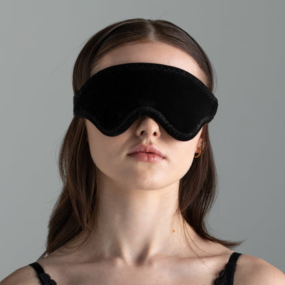 A lady wearing black LoveBlind blindfold by Liberator against a grey background.
