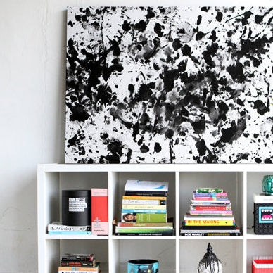 Black and white abstract painting made using the Love is Art Kit displayed above a bookshelf in a living room for modern decor inspiration.