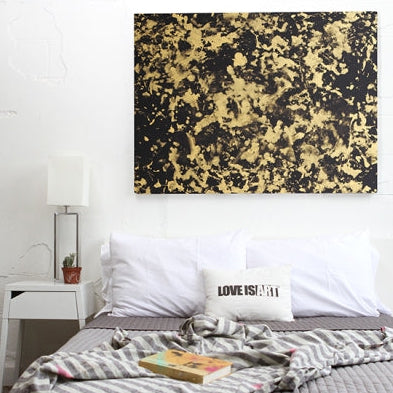 Black and gold Love is Art painting shown framed above a bed in a cozy white bedroom.