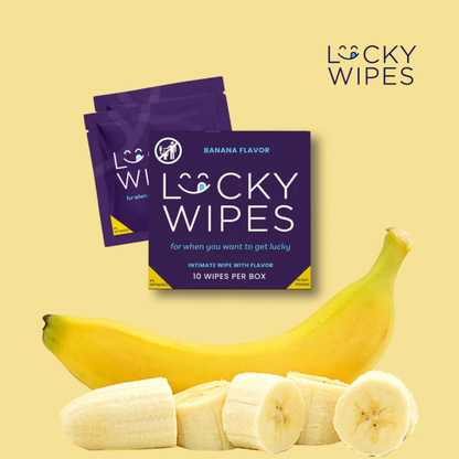 Purple packages of Banana flavored Lucky Wipes for Him sitting next to a pealed and cut banana against a yellow background.