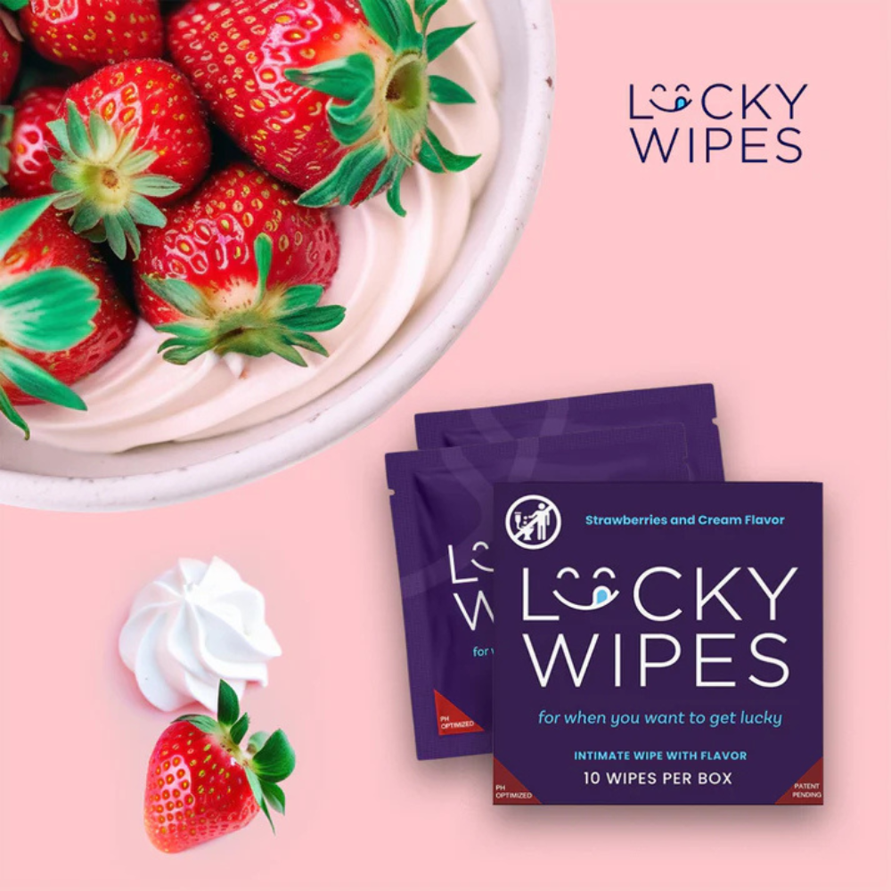 Individual purple packages of Strawberries and Cream flavored Lucky Wipes for Him next to a bowl of strawberries against a pink background.