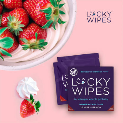 Individual purple packages of Strawberries and Cream flavored Lucky Wipes for Him next to a bowl of strawberries against a pink background.