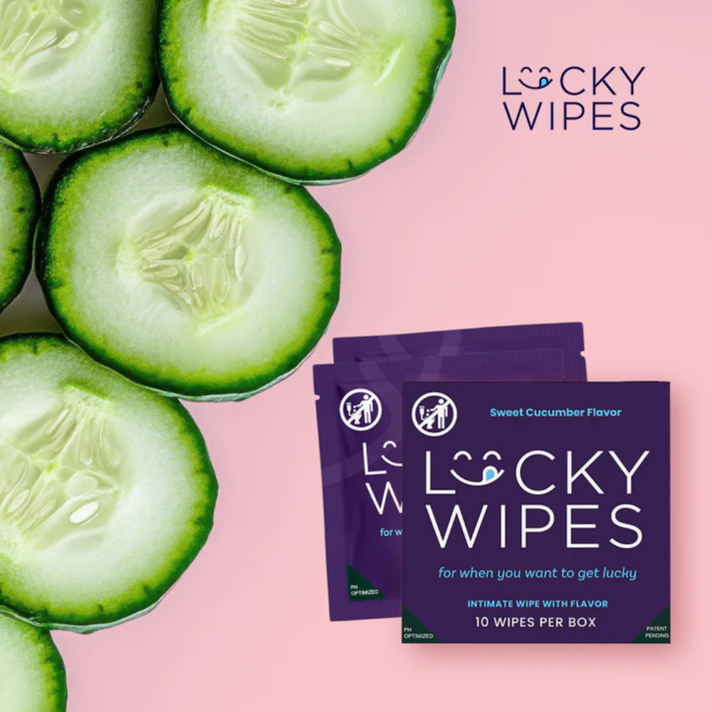 Purple packages of Sweet Cucumber flavored Lucky Wipes for Him next to a cut up cucumber against a pink background.