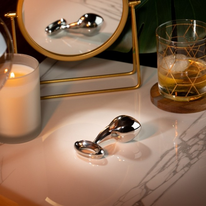 A Luxy Stainless Steel Anal Plug sitting on a table with a mirror and a candle.