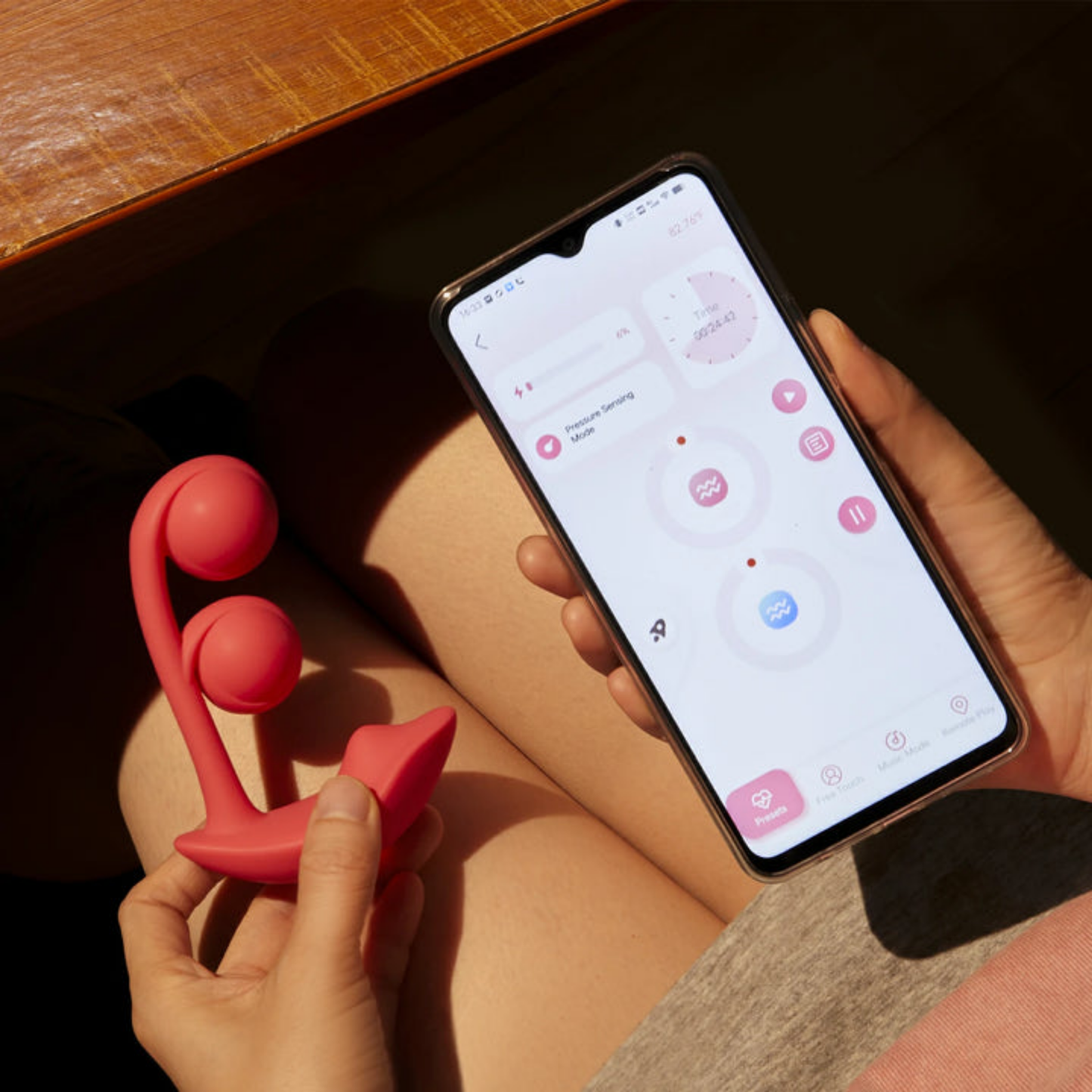 A pink Melody Wearable remote vibrator being held next to a phone showing the app used to control it.