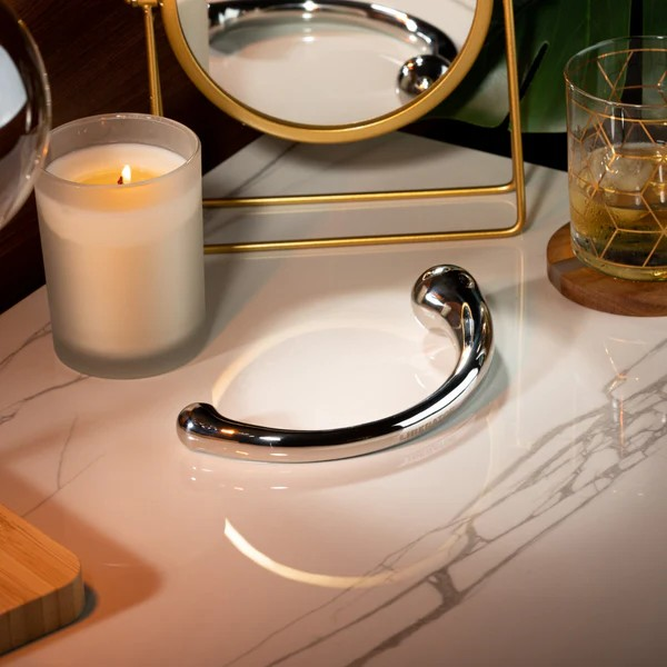 A stainless steel Mezzo wand sitting on a table next to a mirror and a candle.