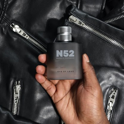 A hand holding a black bottle of N52 Magnetic Pheromone Cologne by Eye of Love sitting with leather in the background.