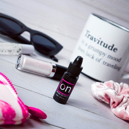 A small black bottle of ON Arousal Original Gel by Sunsuva sitting on a table with sunglasses and a few other things.
