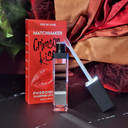 An open tube of lip plumping Crimson Kiss lip gloss by Eye of Love next to the box against a red background.