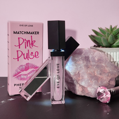 Two pink and silver tubes of pH balanced Pink Pulse lip gloss by Eye of Love against a pink background with the box, a crystal and a plant.