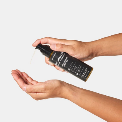 A hand using a bottle of Matchmaker Black Diamond Pheromone Body Oil by Eye of Love against a white background.