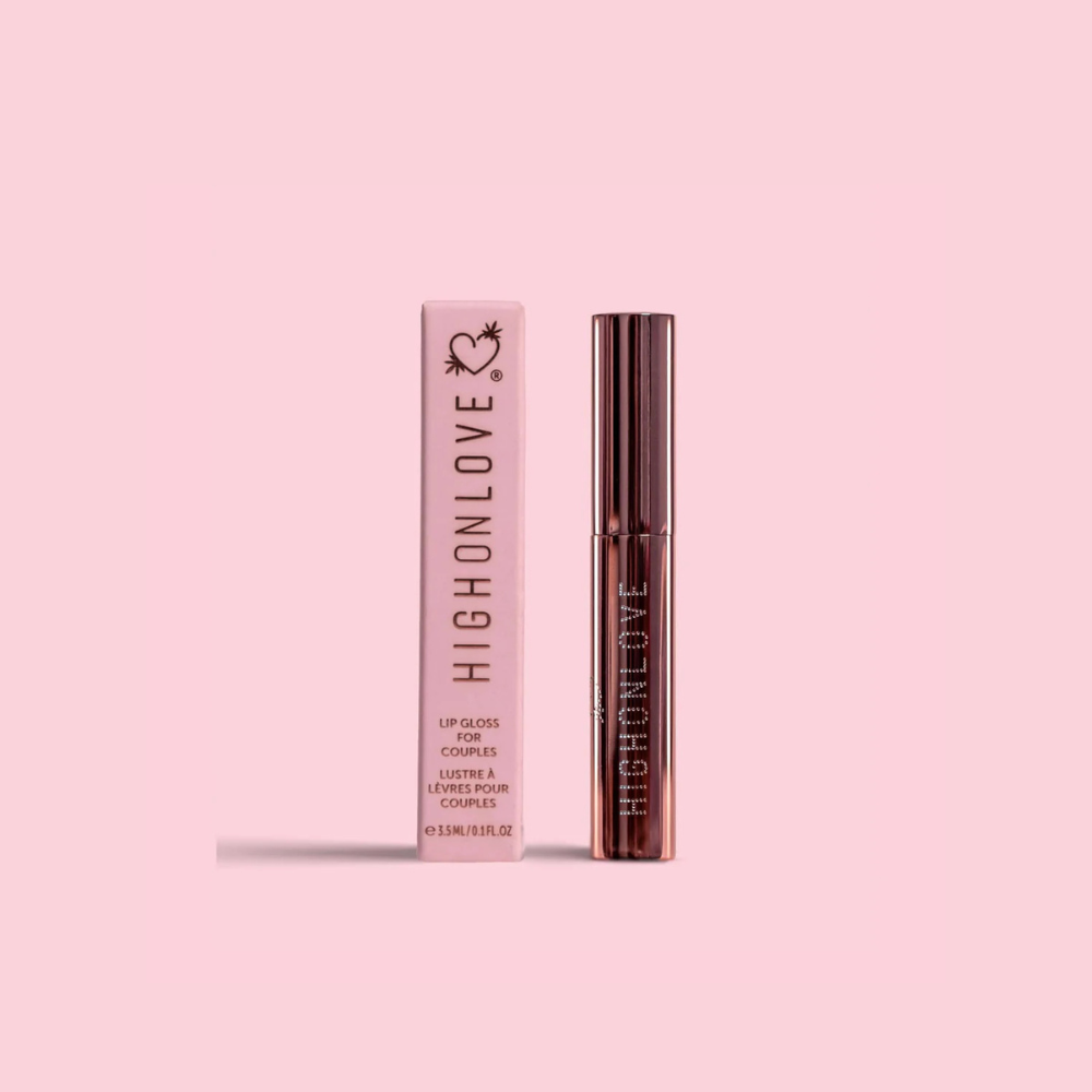 A tube of Plumping Lip Gloss by High On Love sitting next to the box against a pink background.