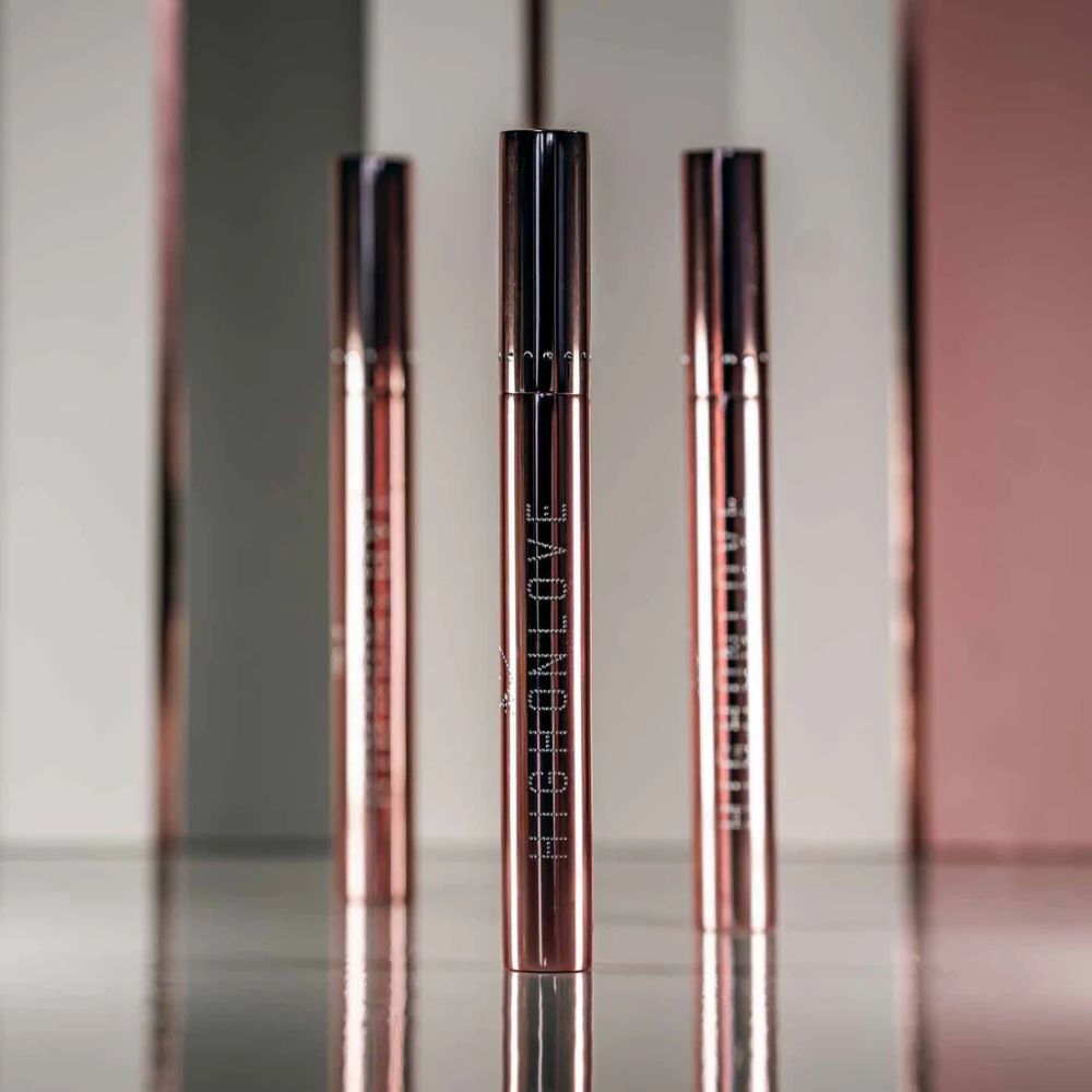 Three tubes of Plumping Lip Gloss by High On Love against a pink and grey background.
