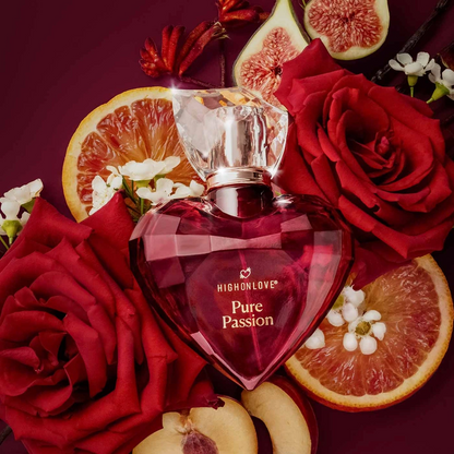 Heart-shaped Pure Passion by High on Love perfume bottle surrounded by red roses, oranges, and figs on a dark background.