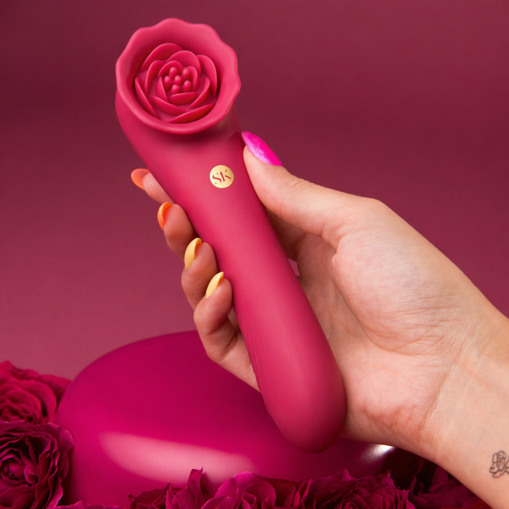 A hand holding red rose colored Rose Quake vibrator with a rose end against a red background.
