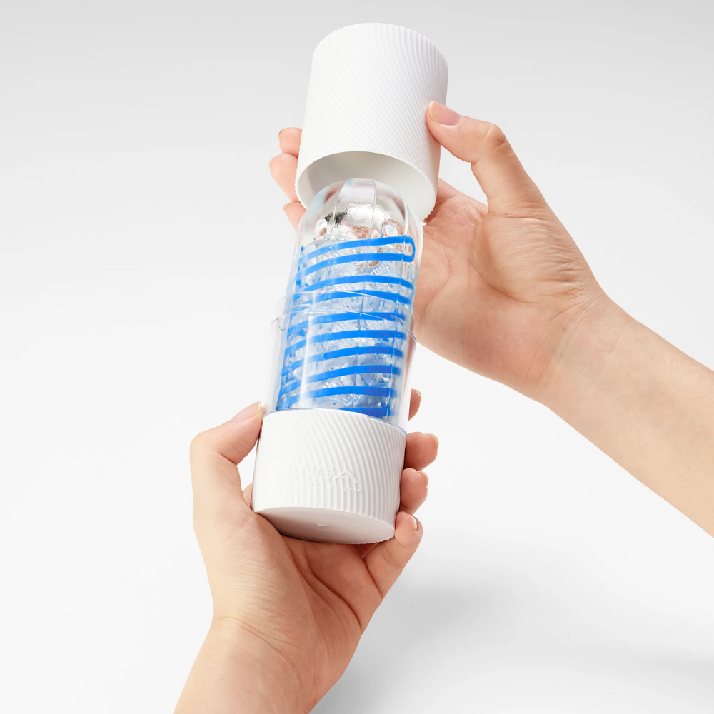 Hand holding a white and blue striped cylindrical product against a light gray background